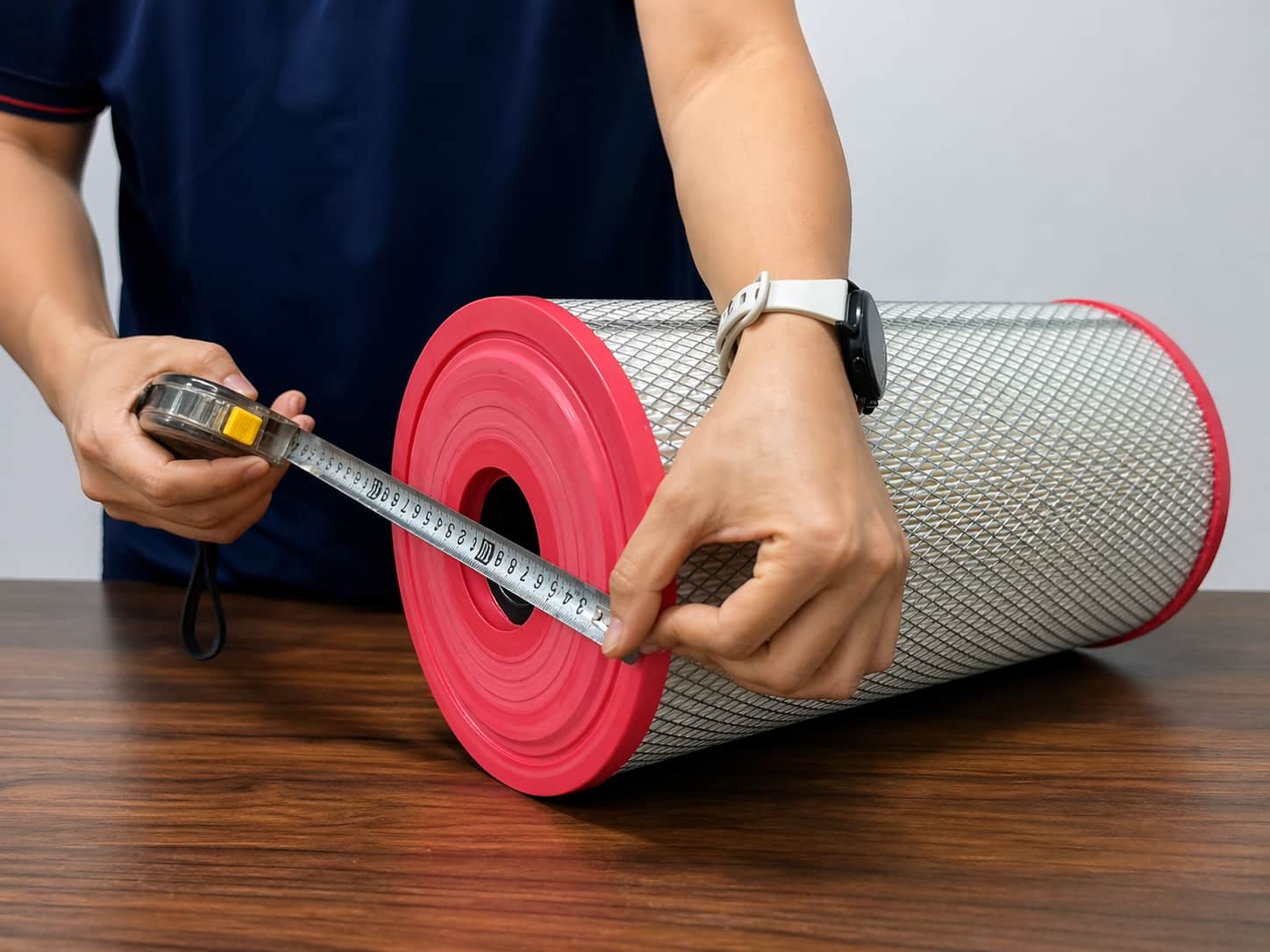 Worker measuring the diameter of a cylindrical air filter on a wooden table