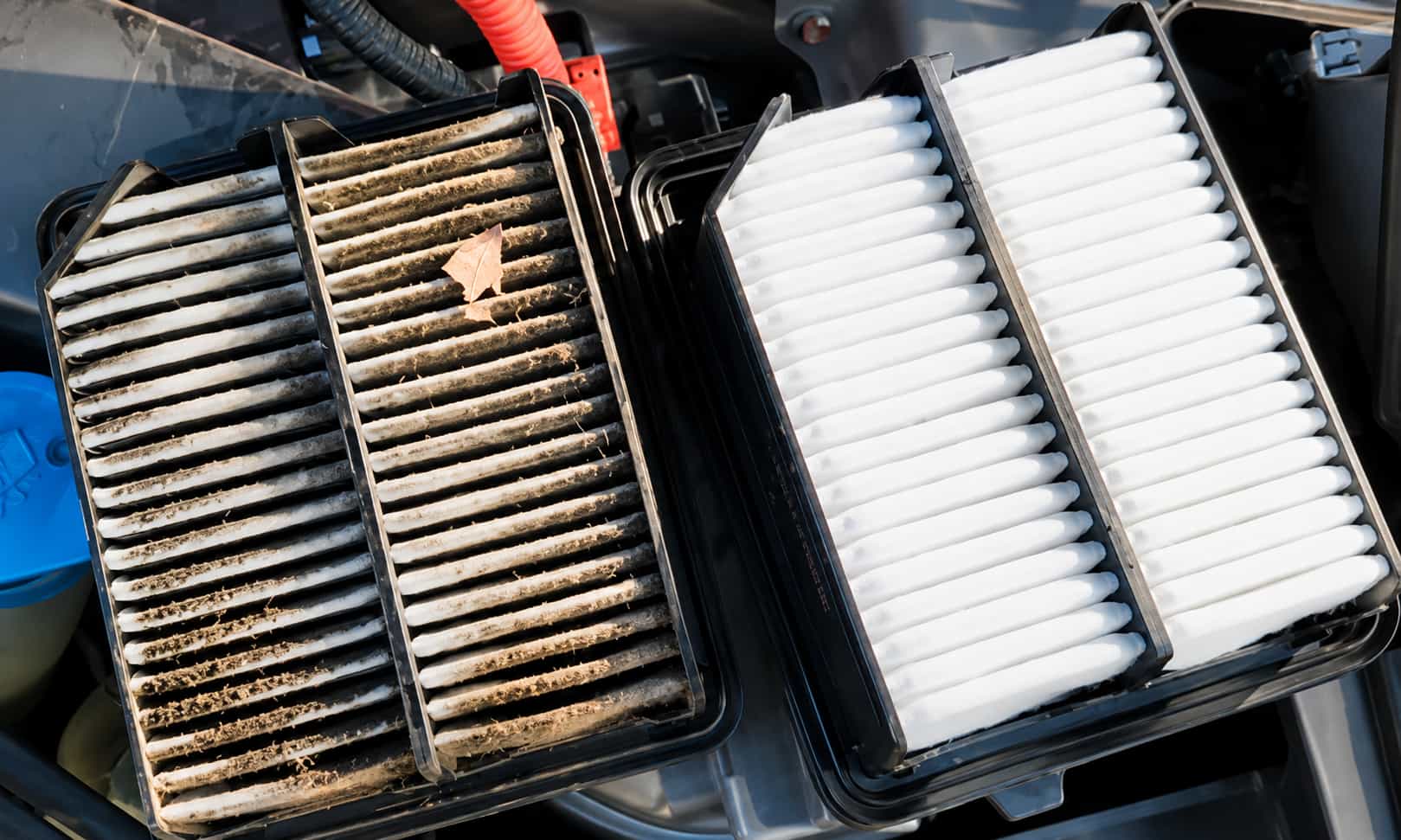 Dirty and clean engine air filters shown side by side inside a vehicle engine compartment