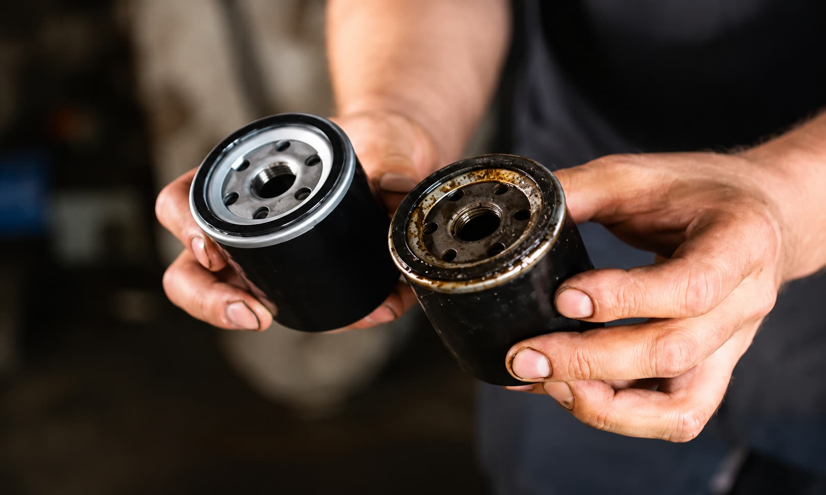 Mechanic holding a clean oil filter and a used oil filter to compare engine oil filter condition