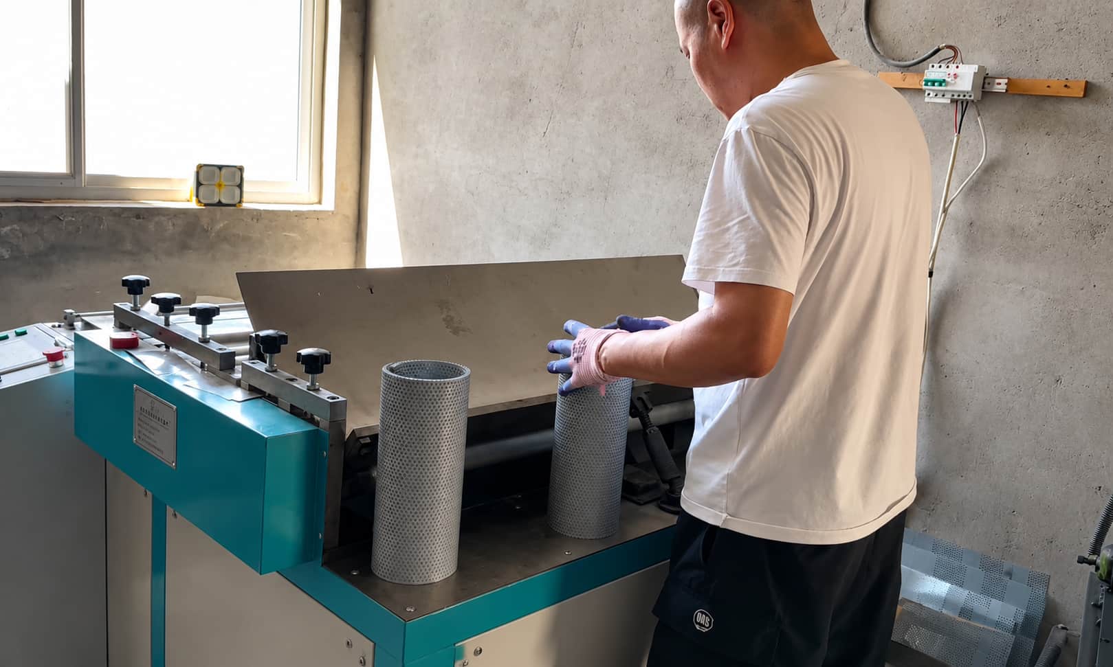 Worker operating automatic metal mesh rolling machine for larger industrial filter support tubes
