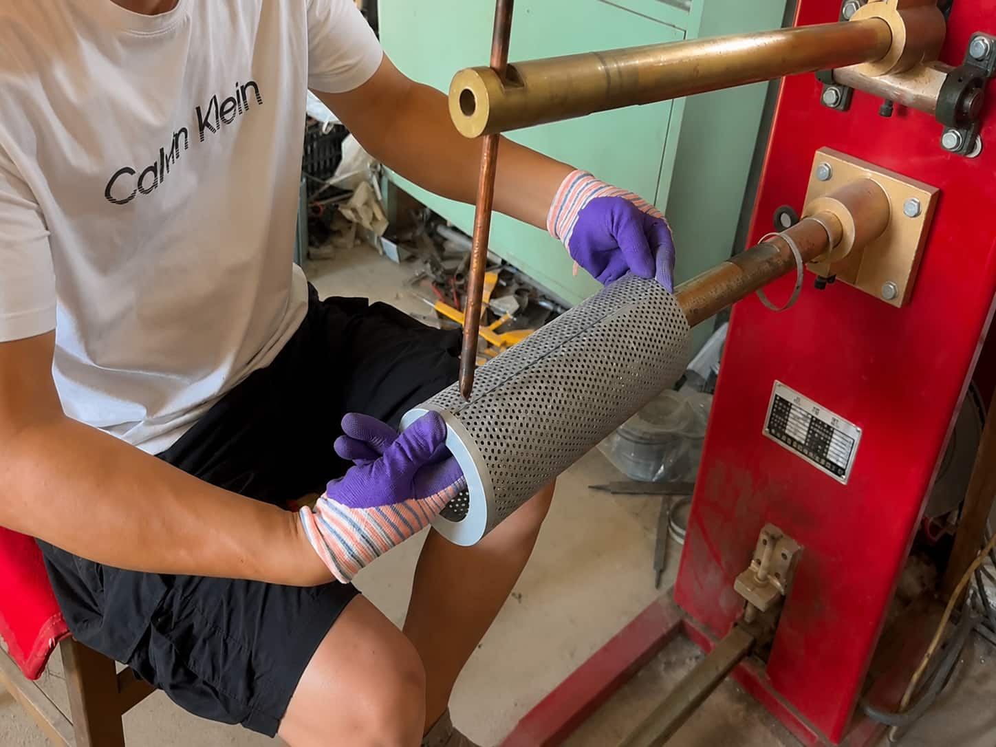Worker welding perforated metal mesh cylinder for industrial filter element support structure